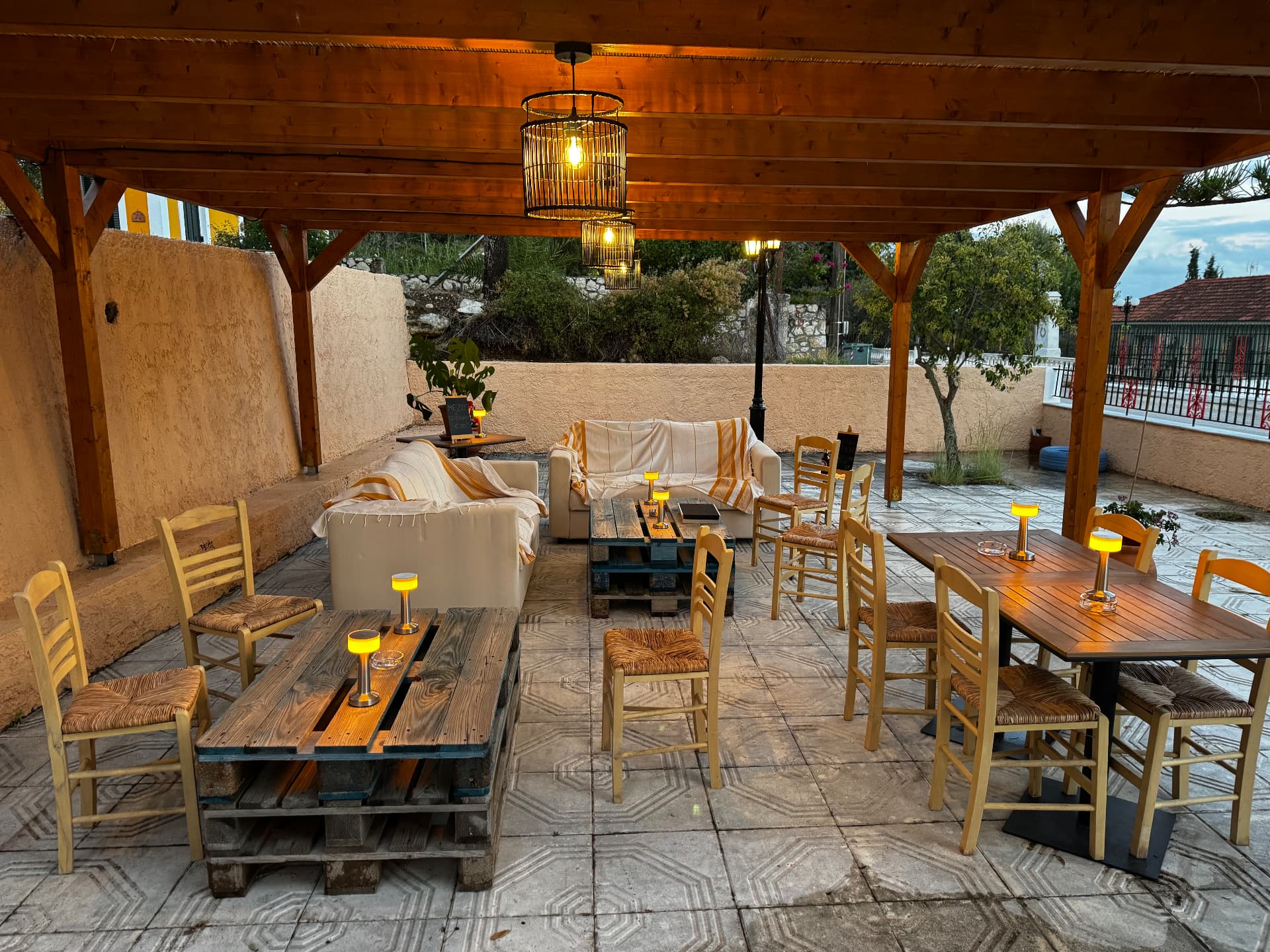 Η σκεπαστή βεράντα του Crazy Horse Café, με ξύλινα τραπέζια, καρέκλες και ζεστό φωτισμό.